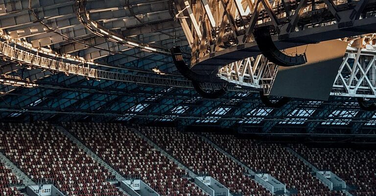 Innenansicht eines großen Stadions mit markanter Dachkonstruktion und leeren roten Sitzreihen.
